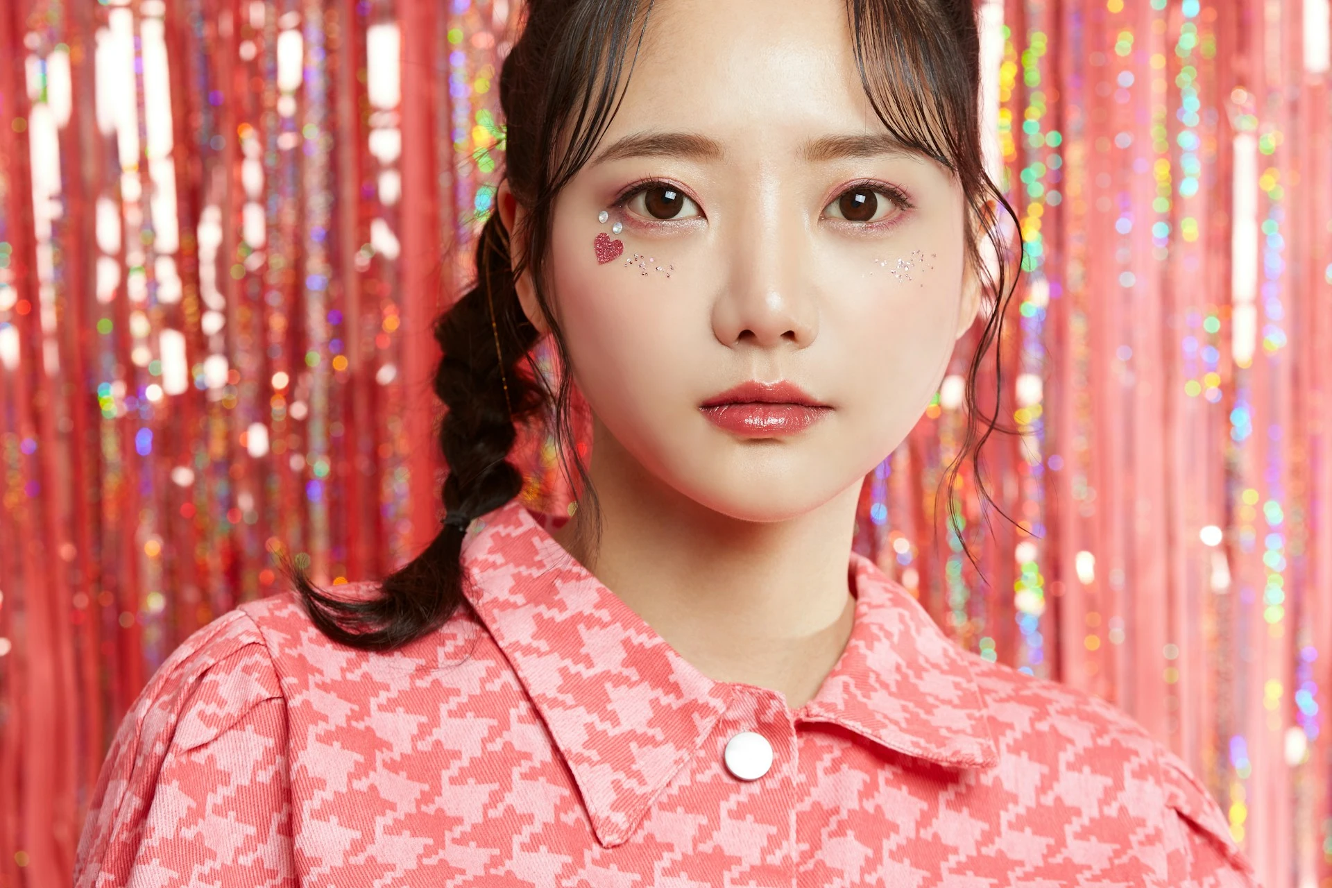 キラキラ光るピンクのフリンジ背景の前で、頬にグリッターメイクを施した女性の近接ポートレート。
